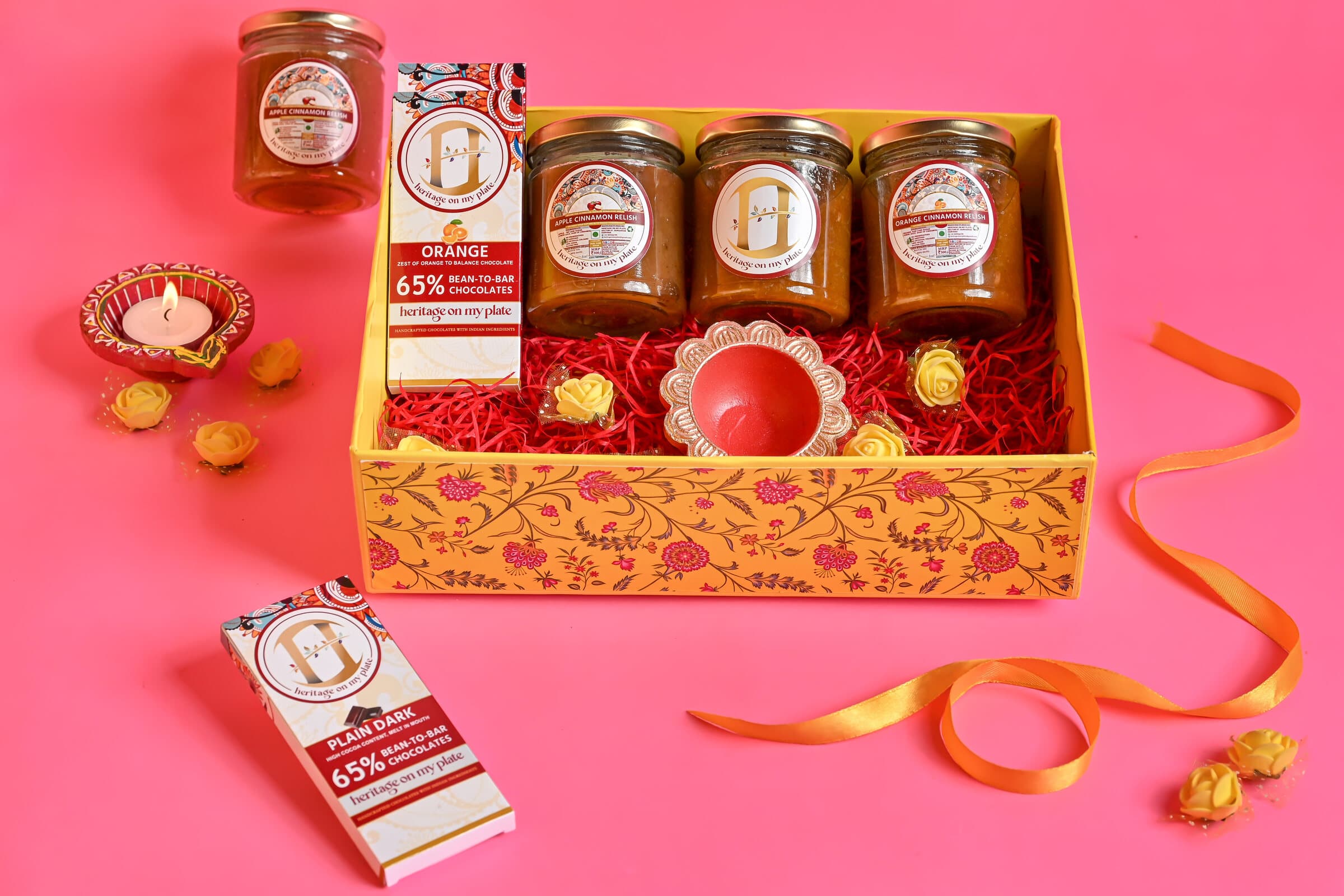 A Diwali hamper of relish jars and chocolate bars with a diya, in a floral gift box