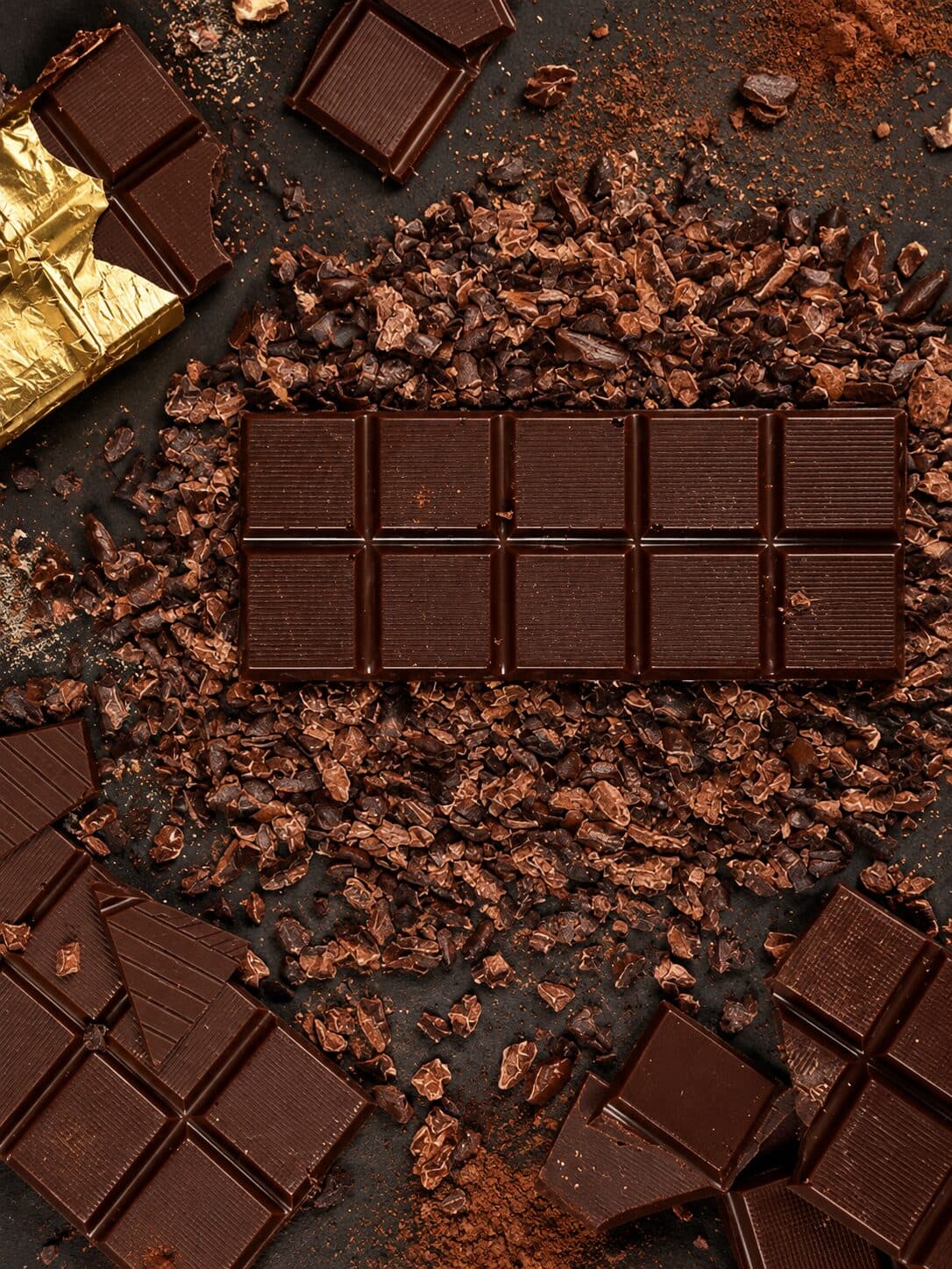 Dark chocolate bars on a bed of roasted cacao nibs, one in gold foil